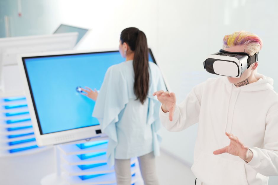 Two young adults engaging with VR and touchscreen technology in a futuristic room.