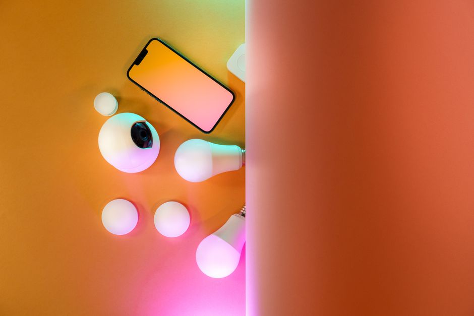 Top view of smart home gadgets including smartphone, camera, and light bulbs in a colorful setup.